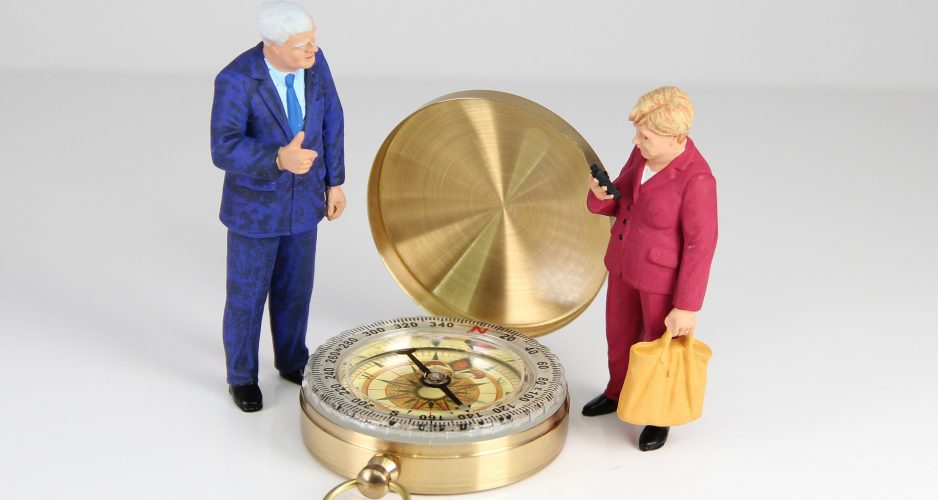Horst Seehofer und Angela Merkel stehen als Spielfiguren neben einem Kompass